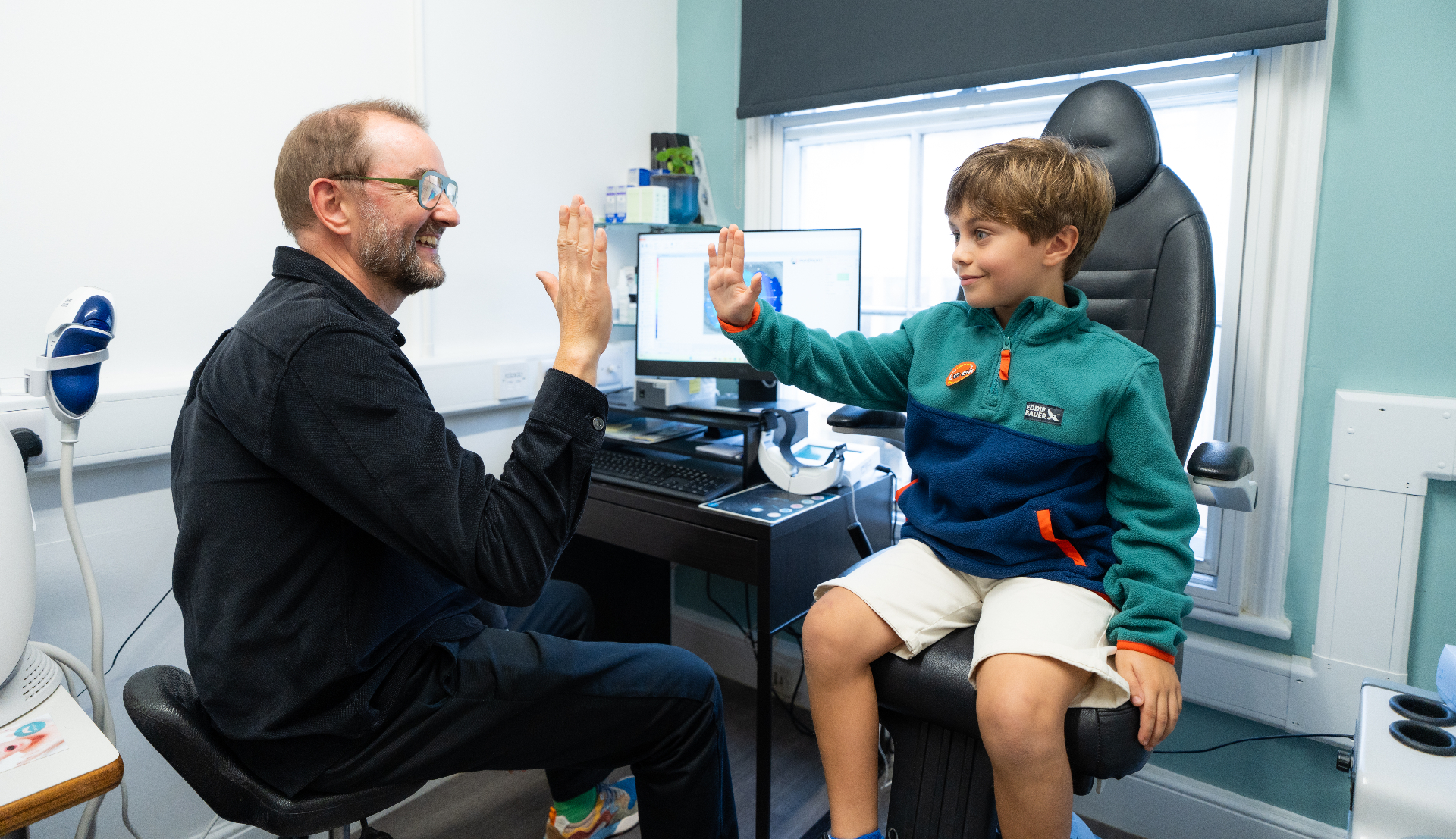 An optician high-fiving a young patient after an eye test